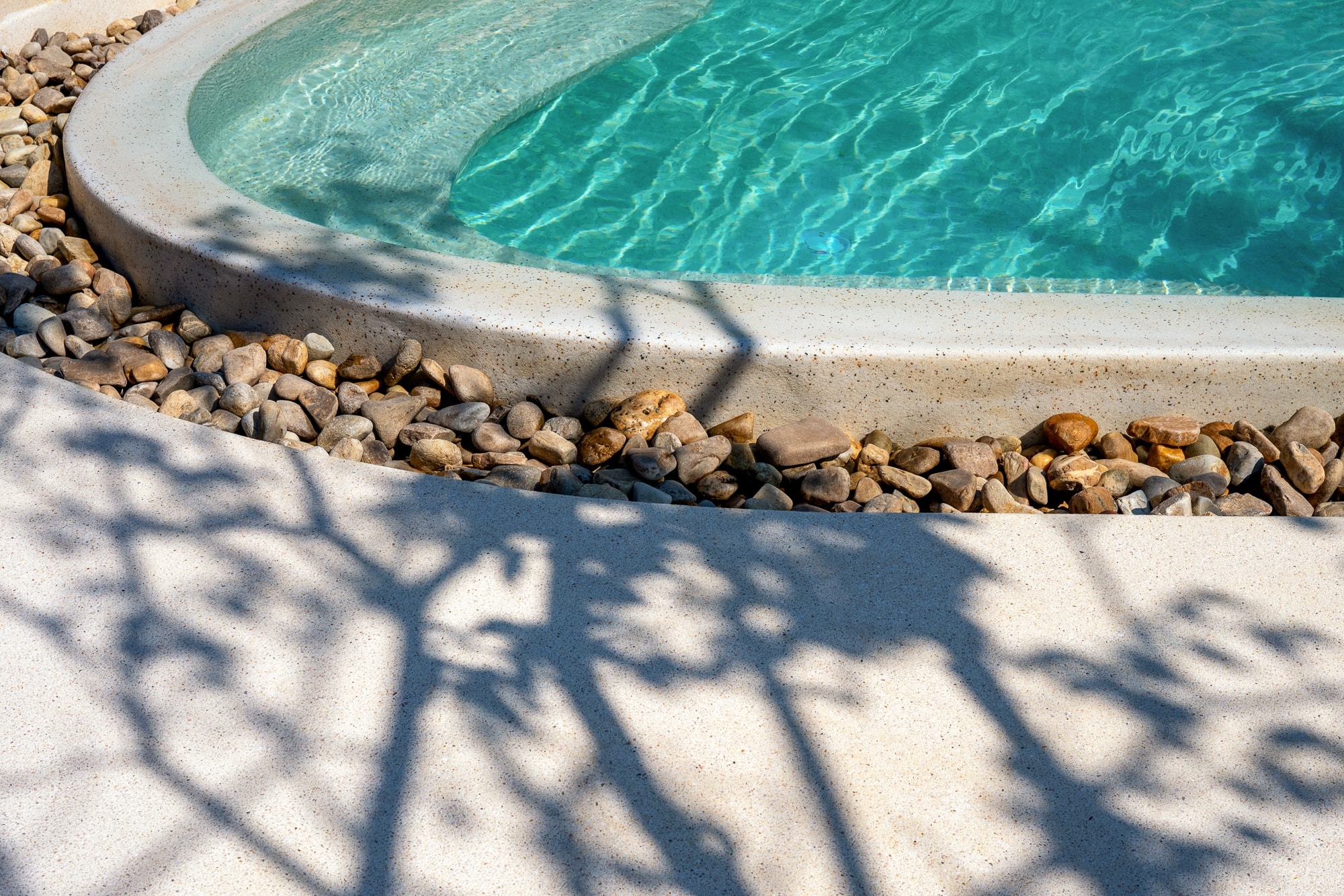Pool edge detail with river stones and tree shadows