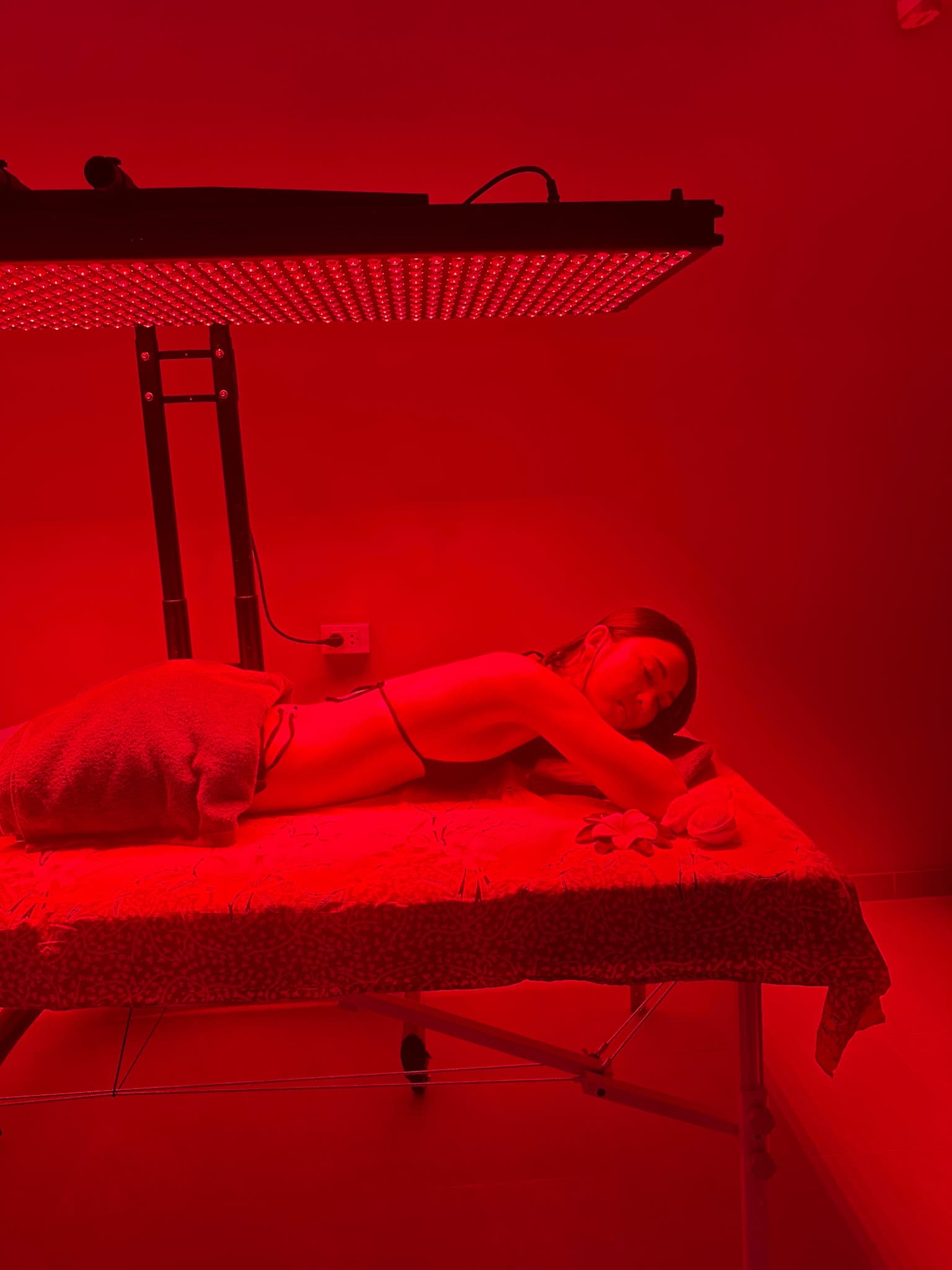 Guest resting face down on the treatment bed beneath the red light panel at BREATHE